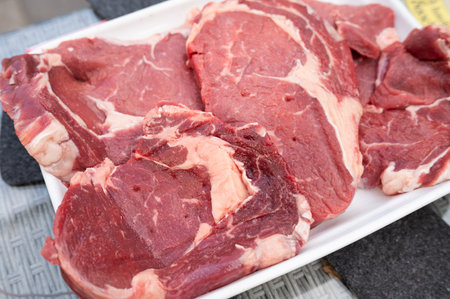 Fresh raw beef steak cuts on tray displayed on outdoor table.