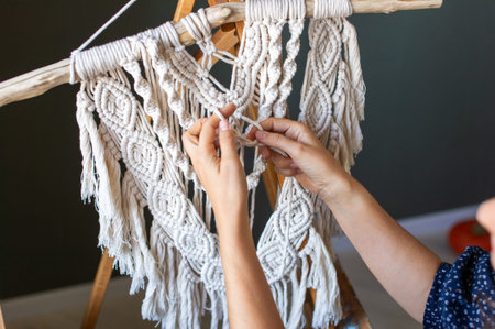 Close-up view of skilled hands intricately weaving a beautiful macrame wall decoration, showcasing craftsmanship and creativityの写真素材