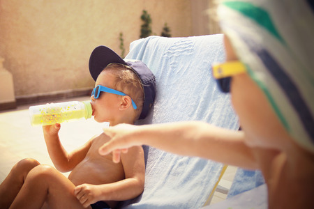 Two cool boys sunbathing near pool with soother