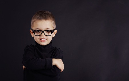 Studio portrait of serious child in black pullover and black glasses on black backgroundの写真素材
