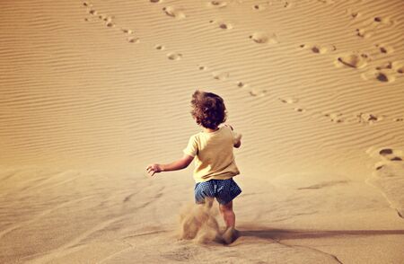 Handsome baby boy walking and playing alone in the desert in Maspalomas, Gran Canaria.の写真素材
