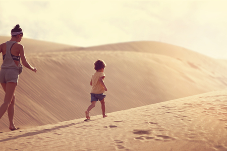 Fit mother with son running at the desert in Gran Canaria, Maspalomas on sunsetの写真素材