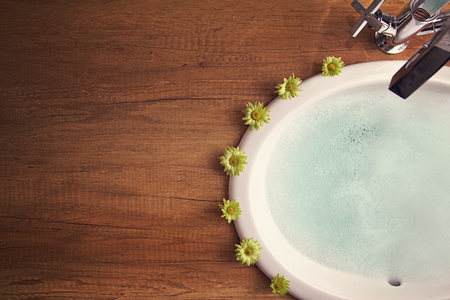 Sink with chome tap on wooden tabletop with blue water and green flowers around.の写真素材