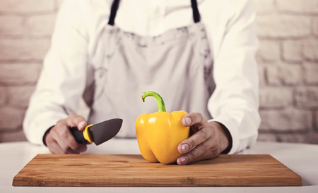 Chef's hands. Man in white clothes and gray apron is ready to prepare fresh salad with pepper,...