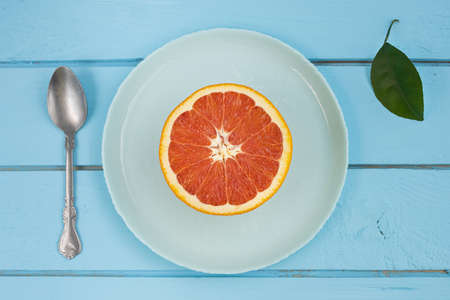Fresh red grapefruit slices on plate with rustic blue wooden background.