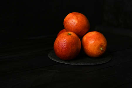 Whole and halved red oranges on black surface.