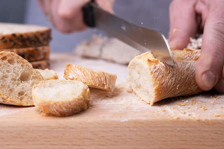 Male hands cutting fresh baguette on the wooden table.