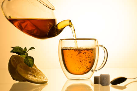 Cup of tea and glass teapot on glass with orange background