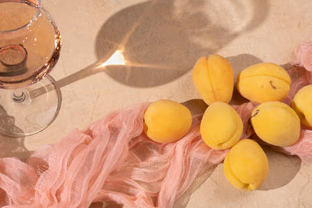Rose wine in a crystal glasses with fresh apricots on on a beige background.の写真素材