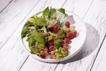 Red berries of wild raspberries in a white plate on a wooden table, a branch of raspberries with...