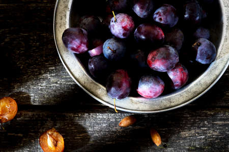Plum in the iron bowl on a wooden backgroundの写真素材
