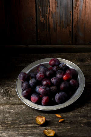 Plum in the iron bowl on a wooden backgroundの写真素材