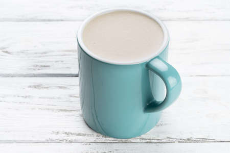 Cup of cappuccino coffee in a blue mug on white wooden backgroundの写真素材