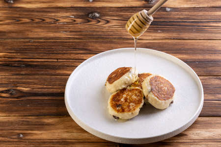cheesecakes on a white plate with honey on wooden backgroundの写真素材