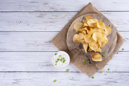 Delicious golden potato chips on a white wooden background.