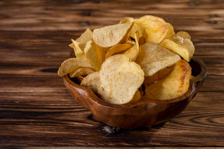 Potato chips on a wooden bowl over wood background