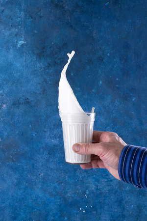 splashes of milk in a glass levitation on a blue background with a hand.