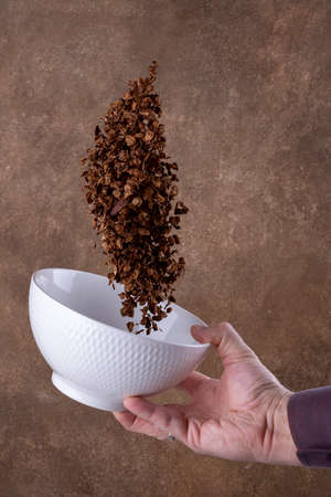 Chocolate corn flakes falling to the white bowl on brown background. Levitation
