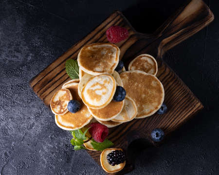 Stack of pancakes with berries on wooden board. Dark wooden background.の写真素材
