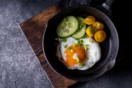 breakfast with fried eggs in a pan with bacon and vegetables on dark background.