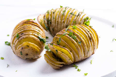 Baked potatoes on on a white plate on white wooden table.