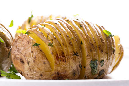 Baked potatoes on on a white plate on white wooden table.