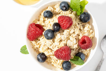 oatmeal with raspberries and blueberries in white bowl on white table. Top viewの写真素材