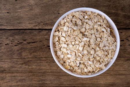 Dry rolled oatmeal in bowl on wooden background. top view