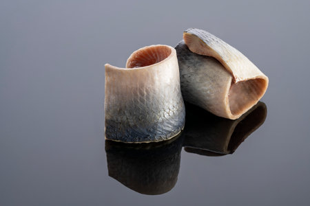 pieces of salted herring fish on a mirror background