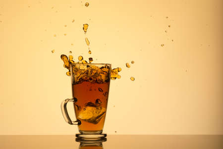 glass of iced tea and splashes on a yellow background with reflection