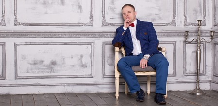 Imposing mature man in elegant suit sitting on a leather chair in a modern luxurious interior. Fashion. Business.の写真素材
