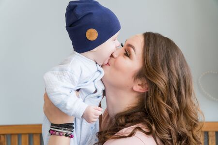 Close-up portrait of happy young mother hugging and kissing his sweet adorable child. Indoors shot, concept image.の写真素材