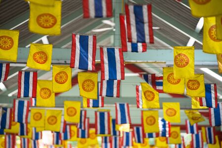 Thai national flag and dharmachakra flag decorated above a walking streetの写真素材