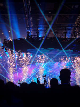 Silhouette people crowd happy and cheering in front of colorful stage with bright blue laser light beam. Music superstar performance. Soft focusの写真素材