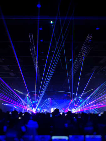 Silhouette people crowd happy and cheering in front of colorful stage with bright blue laser light beam. Music superstar performance. Soft focusの写真素材