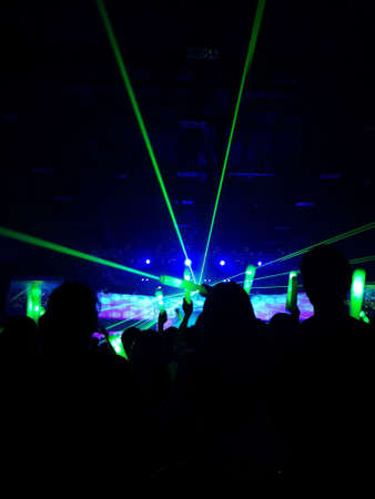 Crowd at concert : Silhouette people crowd happy and cheering with led foam stick light in front of bright colourful stage lights, Green laser light beam.の写真素材