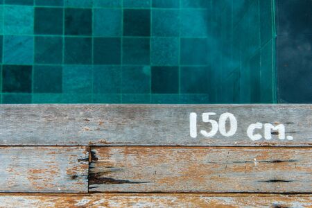 Swimming pool water depth sign on wooden platform, taken on a vertical angle.の写真素材