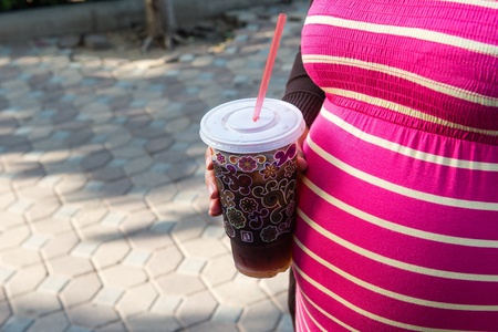 Asian pregnant woman holding a cup of softdrink, taken on a sunny dayの写真素材