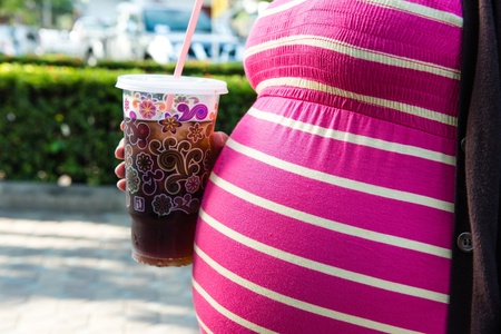 Asian pregnant woman holding a cup of softdrink, taken on a sunny dayの写真素材