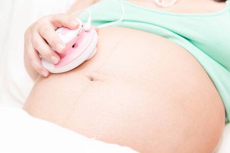 Young thai pregnant woman listening to baby using a listening deviceの写真素材