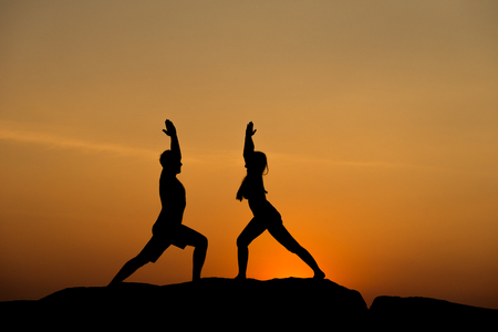 Silhouette of attractive confident half naked man and woman doing yoga on beach rock for wellness yoga zen meditation fitness mind body training, healthy happy relax smile, wonderful sun set beachの写真素材