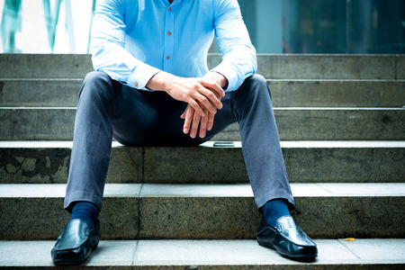 Young business man sitting on stair outdoor in urban city. Man with blue shirt and black pants sit down on concrete stairs outside.の写真素材