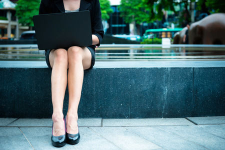 Young business leader agile working concept. Young business woman working outside office in outdoor on sunny day with laptop. Attractive woman with black jacket, skirt, shoes with notebook outdoor.の写真素材