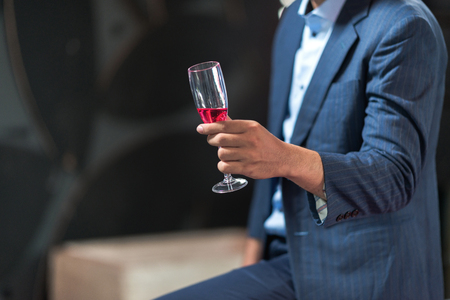 Portrait of young man holding a glass of sparkling rose wine. Handsome chinese single man holding alcoholic beverages with real open air dance club in background. Party concept.の写真素材