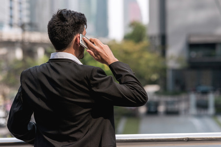Mobile office concept.  Handsome successful white business man or sale man talking on his cell phone with financial building in background. Taken outdoor, apply urban looks effect.の写真素材