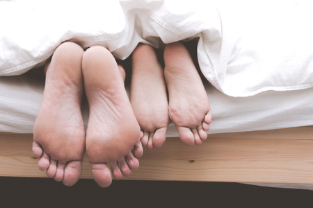 Mixed race lovers concept. Young white male in his bedroom getting intimate with his pretty young chinese girlfriend under the blanket. Wearing blue jeans, shirt and in their early twenties.の写真素材
