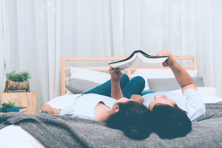 Mixed race lovers concept. Young white male reading a book in his bedroom with his pretty young chinese girlfriend to join. Wearing blue jeans, blue shirt and in their early twenties. Taken indoor.の写真素材