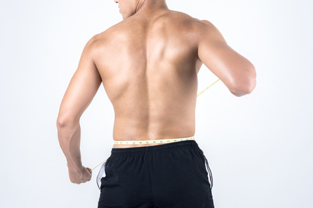 Fitness and health concept. Fit sport man measuring waist to check his body fat amount, isolated on white background. Half naked Asian chinese lean muscular male wearing a black shorts.の写真素材