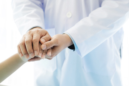 Doctor with patient. Routine health check and holding hands. Male medical doctor with young chinese woman.の写真素材