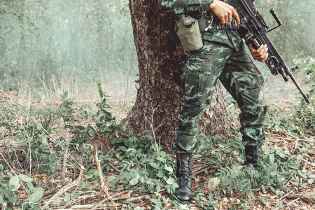 Soldier standing behind a tree ready to attack. Chinese male soldier standing behind a large tree looking around for his ememy.の写真素材